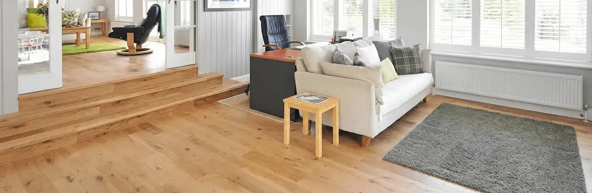 A modern living room with professionally installed laminate flooring, a beige sofa, a small side table, a gray rug, and large windows with white shutters in San Antonio, TX
